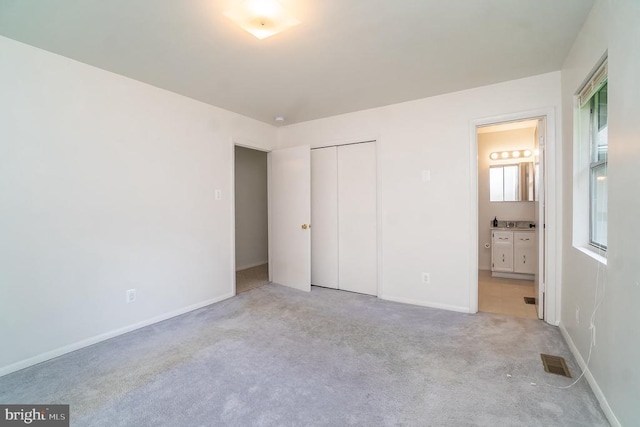 unfurnished bedroom featuring ensuite bathroom, a closet, and light colored carpet