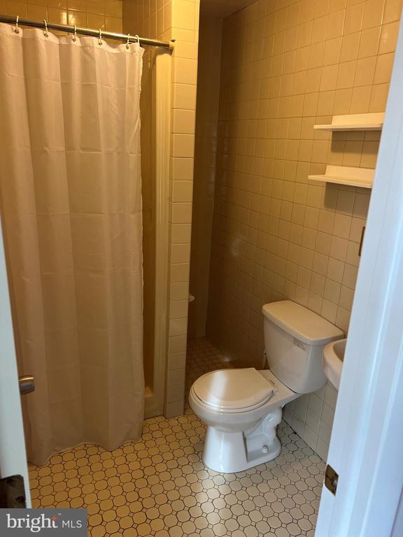 bathroom featuring a shower with curtain, toilet, and tile walls