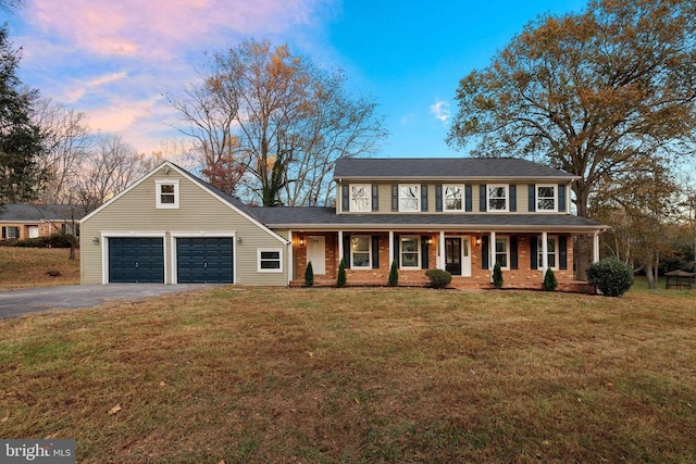 colonial home with a lawn, covered porch, and a garage