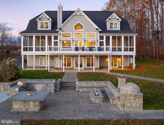 back house at dusk featuring a fire pit, a sunroom, a patio, and french doors