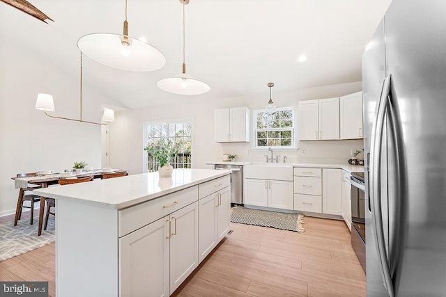 kitchen with a center island, light hardwood / wood-style floors, decorative light fixtures, white cabinets, and appliances with stainless steel finishes