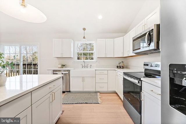 kitchen with hanging light fixtures, sink, light wood-type flooring, appliances with stainless steel finishes, and white cabinetry