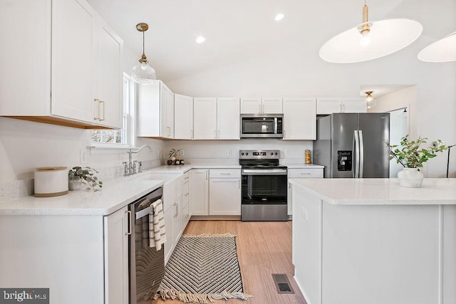 kitchen featuring stainless steel appliances, sink, decorative light fixtures, white cabinets, and light hardwood / wood-style floors