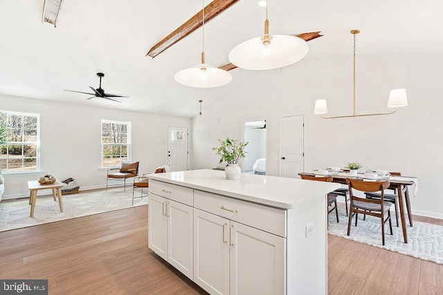 kitchen with ceiling fan, hanging light fixtures, beamed ceiling, white cabinets, and light wood-type flooring