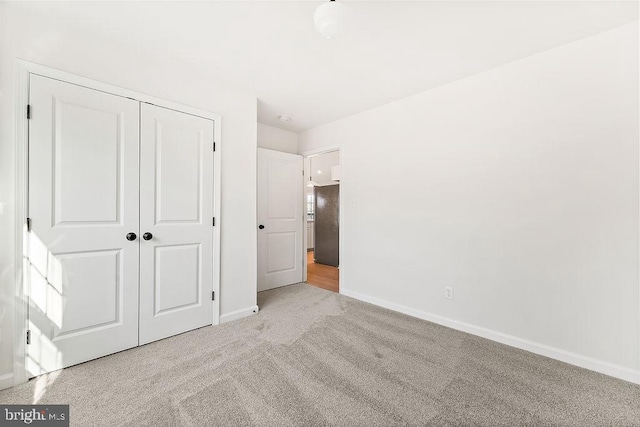 unfurnished bedroom with stainless steel fridge, light colored carpet, and a closet