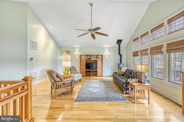 living room featuring a wood stove, ceiling fan, high vaulted ceiling, and light wood-type flooring