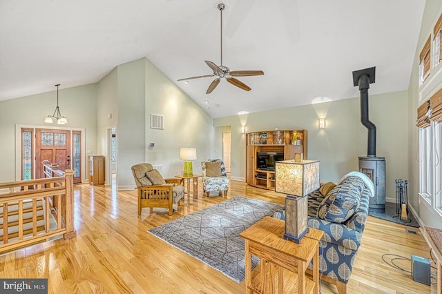 living room with ceiling fan, light wood-type flooring, a wood stove, and high vaulted ceiling