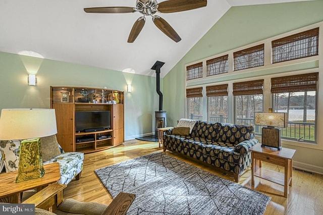 living room with a wood stove, ceiling fan, light hardwood / wood-style flooring, and vaulted ceiling