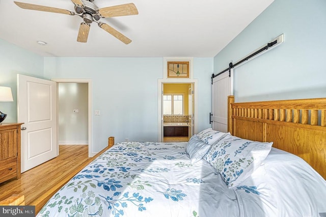 bedroom featuring ceiling fan, a barn door, light wood-type flooring, and ensuite bath