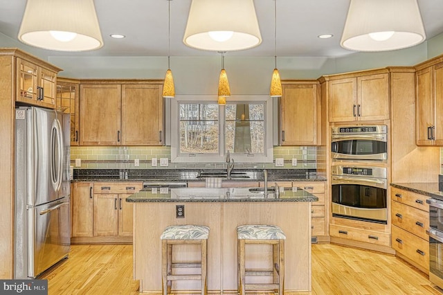 kitchen with dark stone countertops, stainless steel appliances, a breakfast bar area, and an island with sink