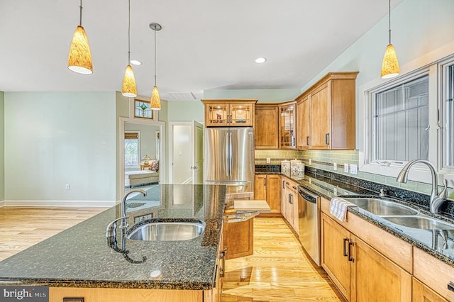 kitchen with sink, a center island with sink, hanging light fixtures, and appliances with stainless steel finishes