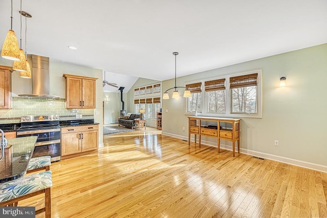 kitchen featuring wall chimney exhaust hood, tasteful backsplash, pendant lighting, stainless steel electric range, and light wood-type flooring