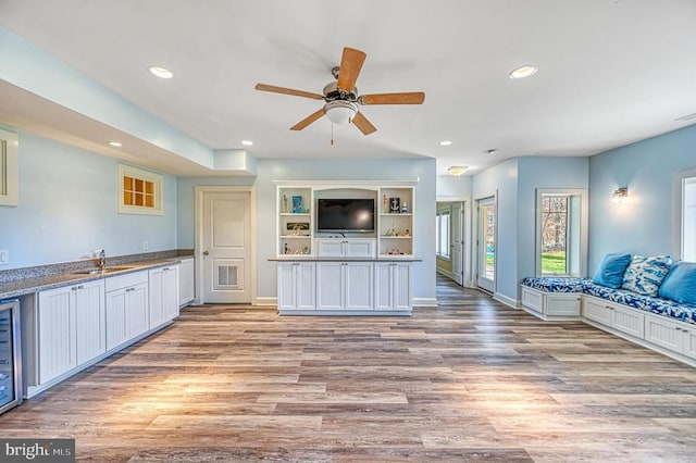 kitchen with white cabinets, light wood-type flooring, light stone countertops, and sink