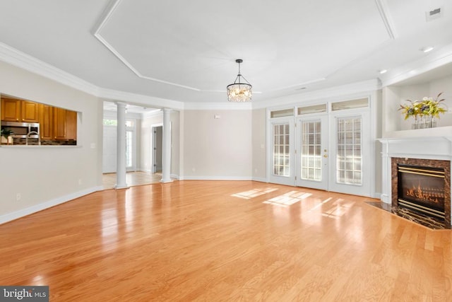 unfurnished living room with crown molding, a premium fireplace, light wood-type flooring, ornate columns, and a chandelier