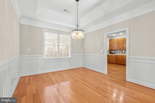 unfurnished dining area with a raised ceiling, crown molding, a chandelier, and light hardwood / wood-style floors