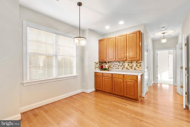 kitchen with tasteful backsplash, hanging light fixtures, a notable chandelier, and light hardwood / wood-style floors