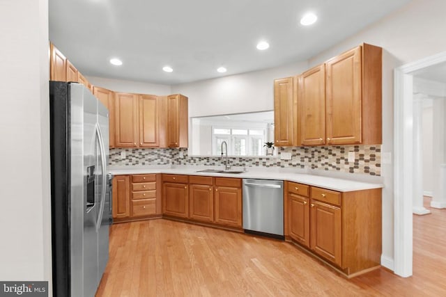 kitchen with appliances with stainless steel finishes, backsplash, light hardwood / wood-style flooring, and sink