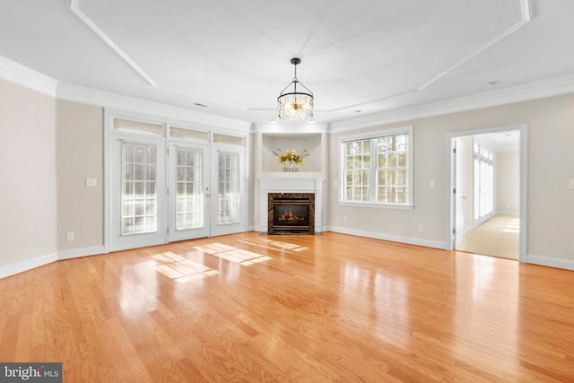 unfurnished living room with a high end fireplace, a raised ceiling, crown molding, a chandelier, and light hardwood / wood-style floors