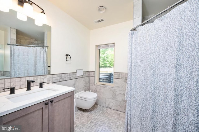 bathroom with tile patterned floors, walk in shower, vanity, tile walls, and toilet