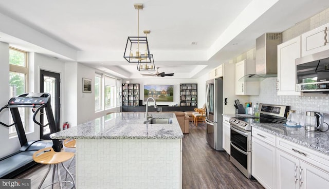 kitchen with pendant lighting, wall chimney range hood, sink, white cabinetry, and stainless steel appliances