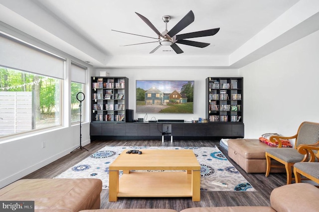 living room with dark hardwood / wood-style floors, ceiling fan, and a raised ceiling