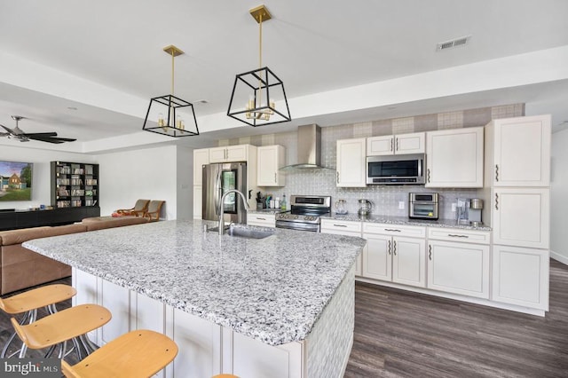 kitchen with stainless steel appliances, ceiling fan, sink, wall chimney range hood, and hanging light fixtures