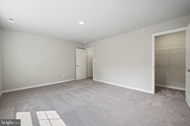 unfurnished bedroom featuring a walk in closet, recessed lighting, carpet, baseboards, and visible vents