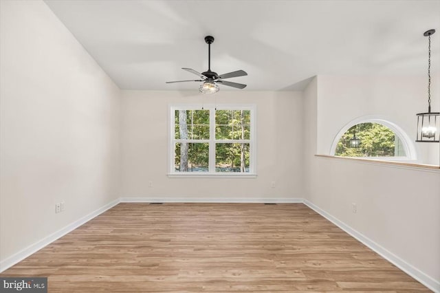 spare room featuring light wood-type flooring and ceiling fan with notable chandelier