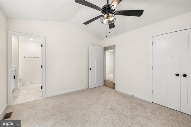 unfurnished bedroom with light carpet, ensuite bathroom, vaulted ceiling, ceiling fan, and a closet