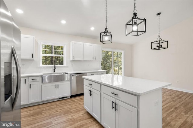 kitchen with stainless steel appliances, a kitchen island, sink, pendant lighting, and white cabinetry