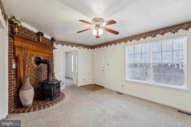 unfurnished living room with ceiling fan, a wood stove, and light carpet