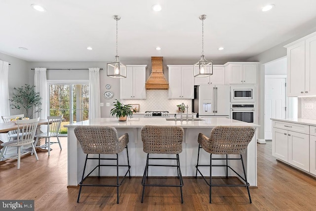 kitchen with pendant lighting, premium appliances, an island with sink, and custom exhaust hood