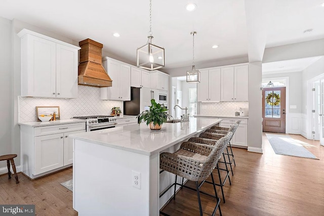 kitchen with high quality appliances, white cabinetry, and an island with sink