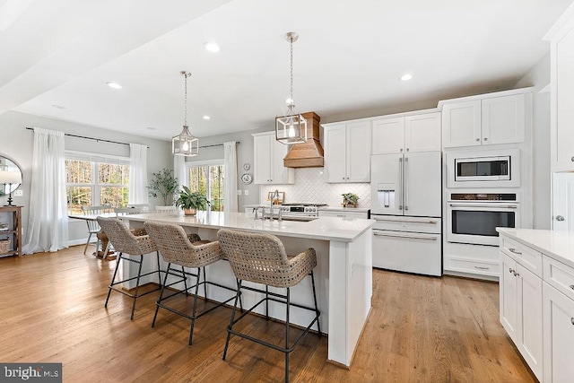 kitchen with built in microwave, oven, pendant lighting, a center island with sink, and white cabinets