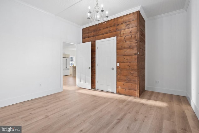 spare room with ornamental molding, a notable chandelier, and light wood-type flooring