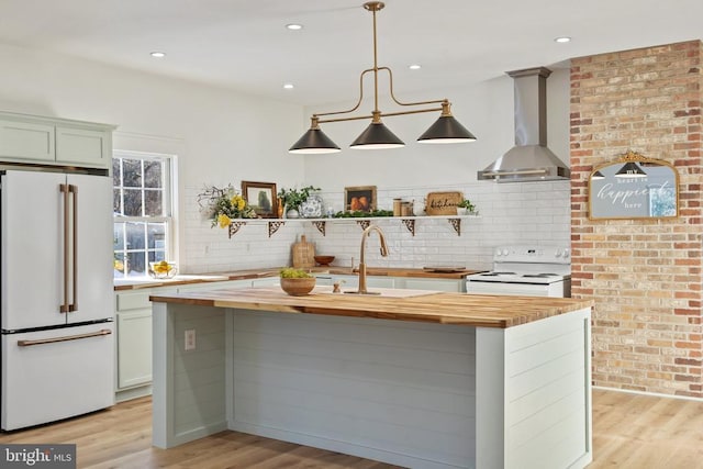 kitchen featuring wooden counters, light wood-type flooring, white appliances, wall chimney range hood, and hanging light fixtures