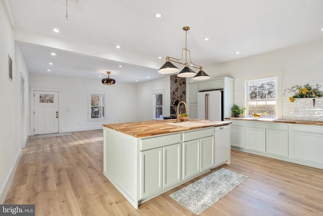 kitchen with white appliances, a center island with sink, light wood-type flooring, decorative light fixtures, and butcher block counters