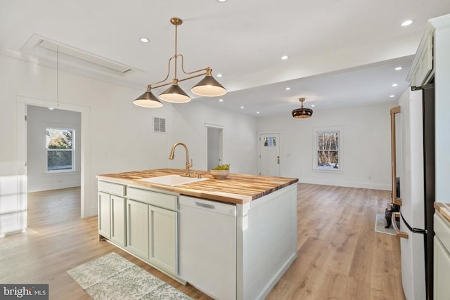 kitchen featuring white appliances, a kitchen island with sink, sink, decorative light fixtures, and butcher block countertops