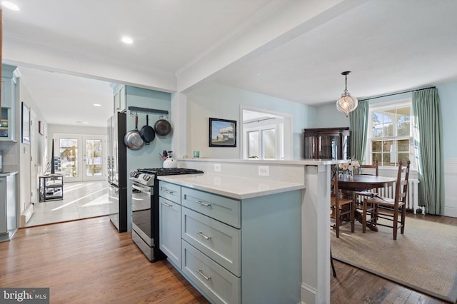 kitchen with appliances with stainless steel finishes, hanging light fixtures, ornamental molding, hardwood / wood-style flooring, and a breakfast bar area