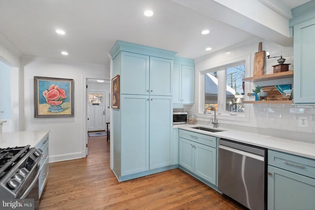 kitchen with light wood-type flooring, appliances with stainless steel finishes, ornamental molding, and sink