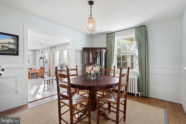 dining area with wood-type flooring, an inviting chandelier, and radiator heating unit