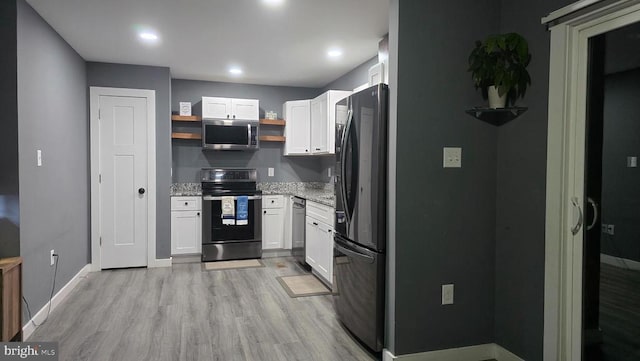 kitchen with light wood-type flooring, stainless steel appliances, white cabinets, and light stone counters