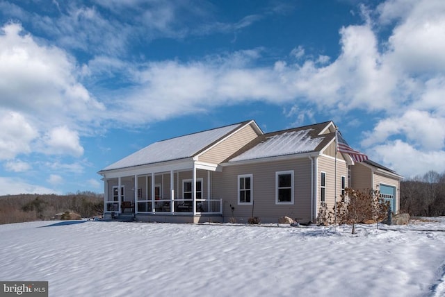 snow covered back of property featuring a sunroom and a garage