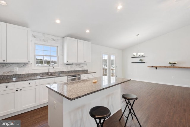 kitchen featuring dishwasher, sink, pendant lighting, dark stone counters, and white cabinets