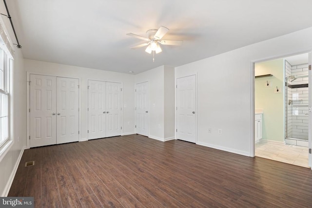 unfurnished bedroom with ensuite bath, ceiling fan, multiple closets, and dark hardwood / wood-style floors