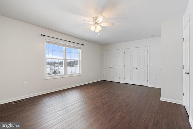 unfurnished bedroom featuring ceiling fan, dark wood-type flooring, and two closets