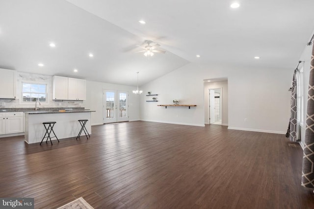 unfurnished living room with ceiling fan with notable chandelier, dark hardwood / wood-style flooring, vaulted ceiling, and sink