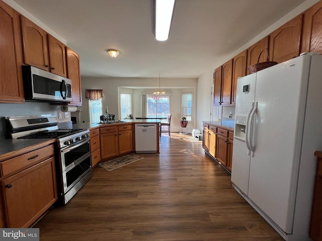 kitchen with kitchen peninsula, stainless steel appliances, a chandelier, dark hardwood / wood-style floors, and hanging light fixtures