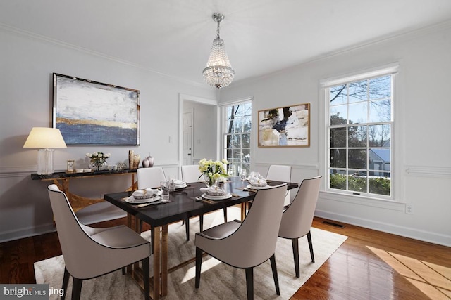 dining space with ornamental molding, a notable chandelier, a wealth of natural light, and hardwood / wood-style floors