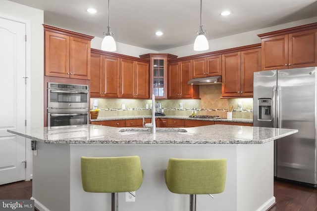 kitchen with appliances with stainless steel finishes, a kitchen island with sink, sink, decorative light fixtures, and a breakfast bar area